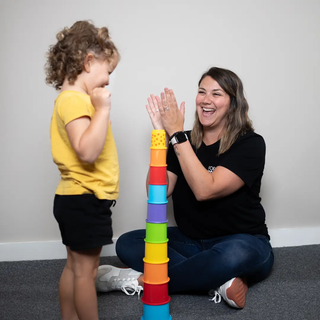 Ashley Maturo sitting on the ground providing speech therapy for kids while playing with stacking cups