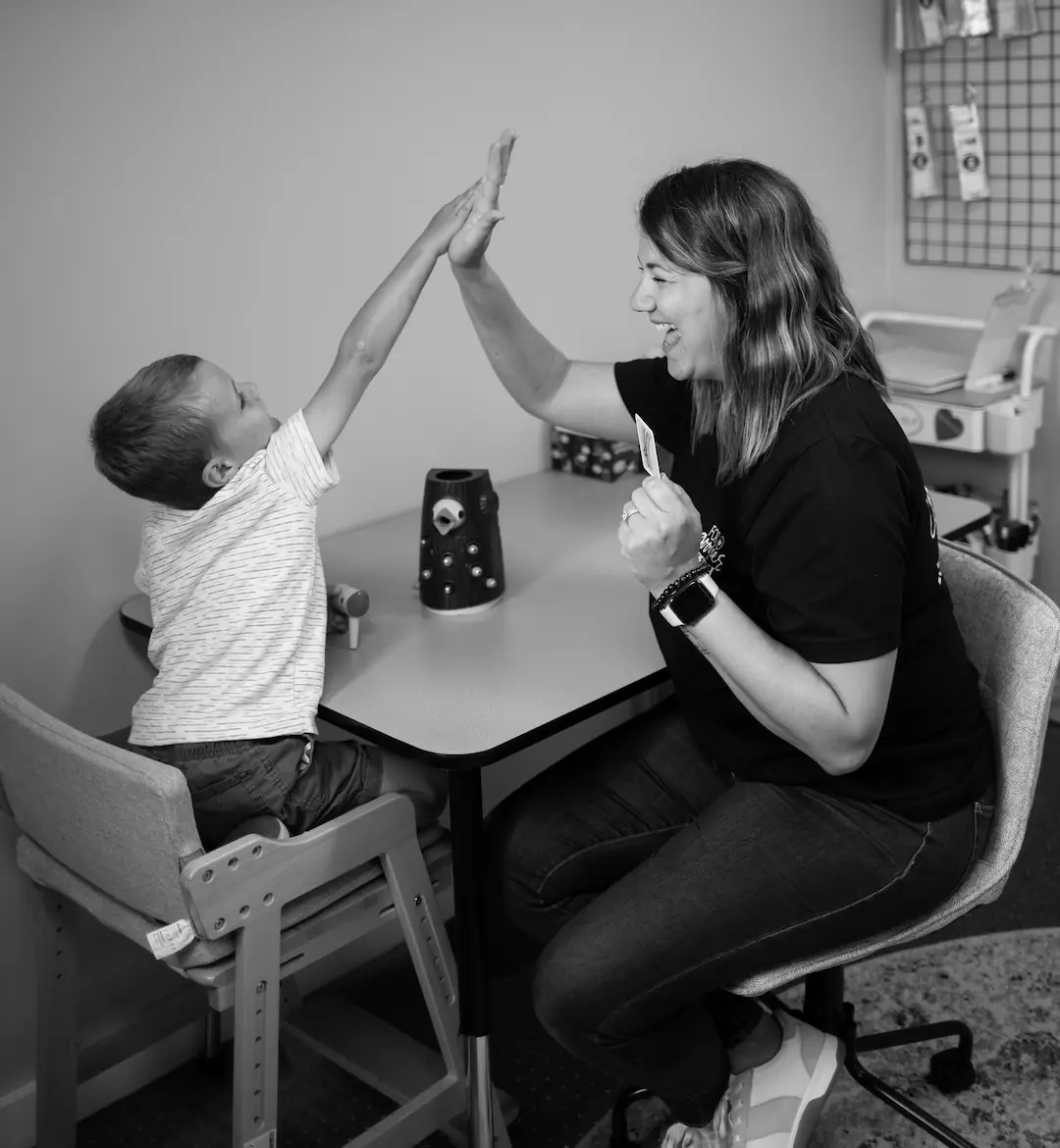 C1NP6581 (2) Ashley Maturo, providing pediatric speech therapy to child while sitting at a table giving a high five
